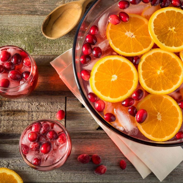 wassail punch in a bowl with fresh cranberries and orange slices beside two glass of punch on a wooden table.