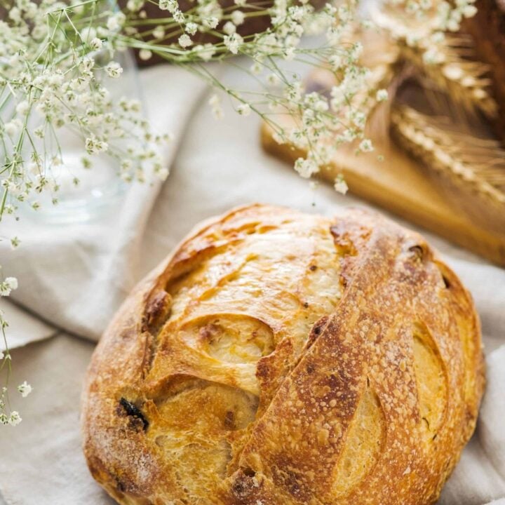 Close up of freshly baked sourdough bread on a linen cloth with white flowers and bread in the background.
