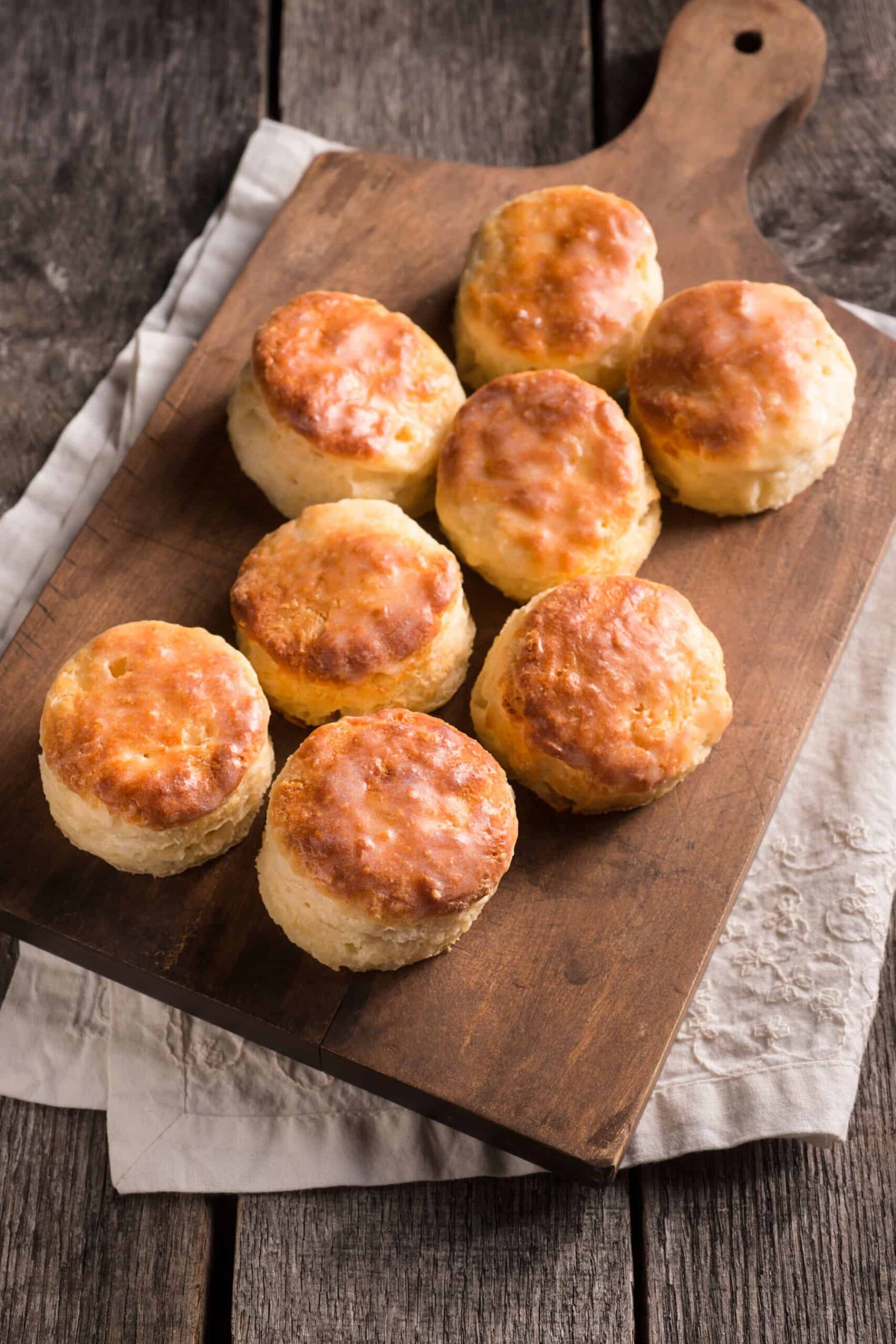 Fresh milled flour biscuits on a wooden cutting board with a tea towel beneath.