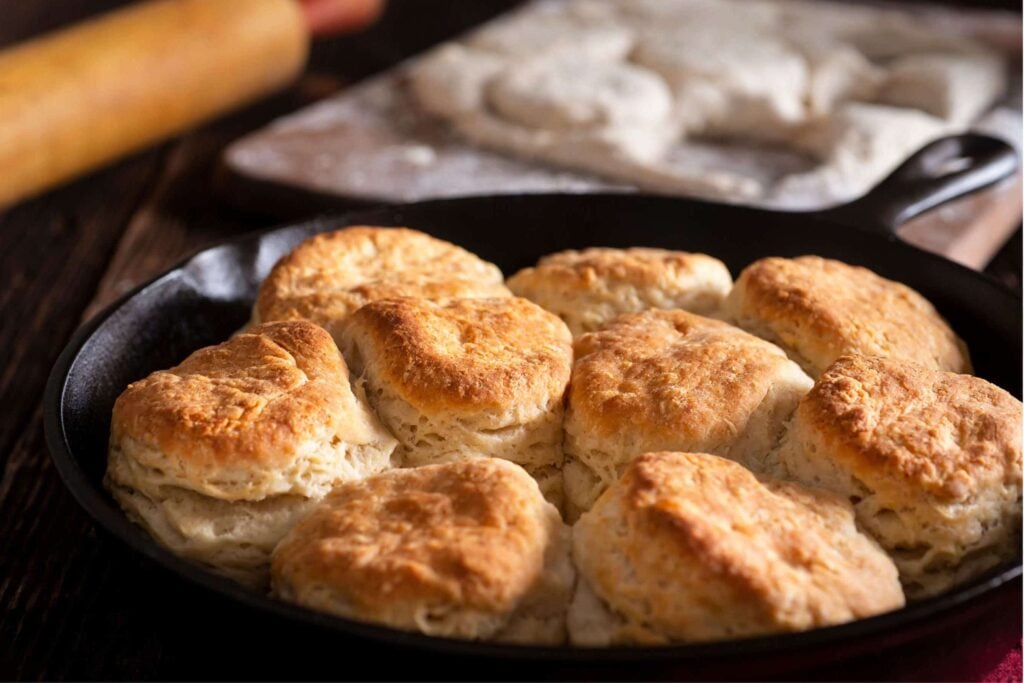 fresh milled flour biscuits just baked in a cast iron skillet with more unbaked biscuits in the background.