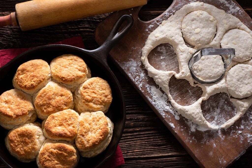 Freshly baked biscuits in a cast iron skillet with unbaked ones beside