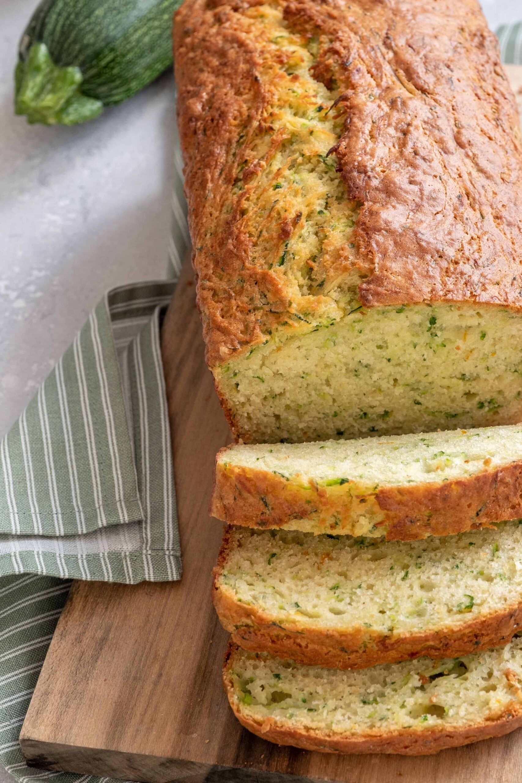 Homemade whole wheat zucchini bread with a tea towel and fresh zucchini.