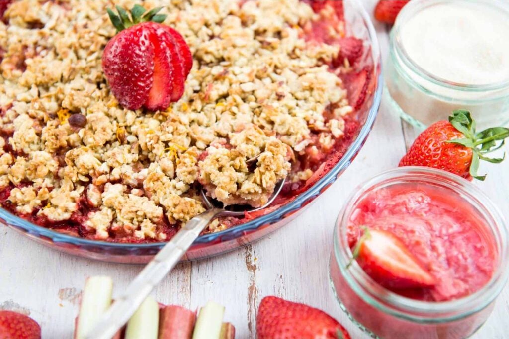 Rhubarb crunch with strawberries and oats on a white table with ingredients beside it.