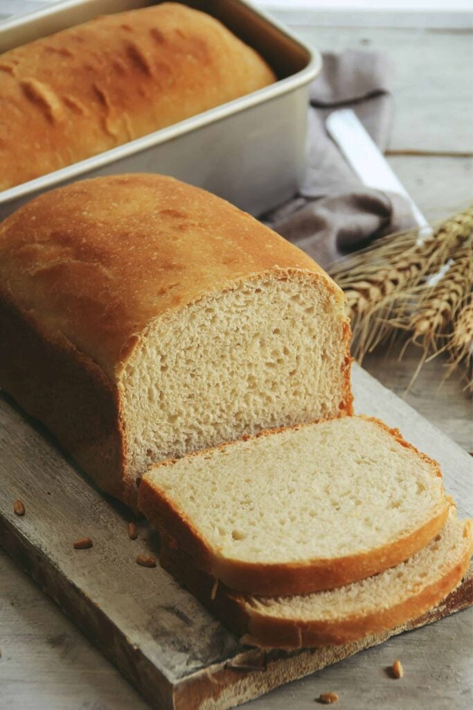 Fresh milled bread on a cutting board with another loaf in a pan behind it.