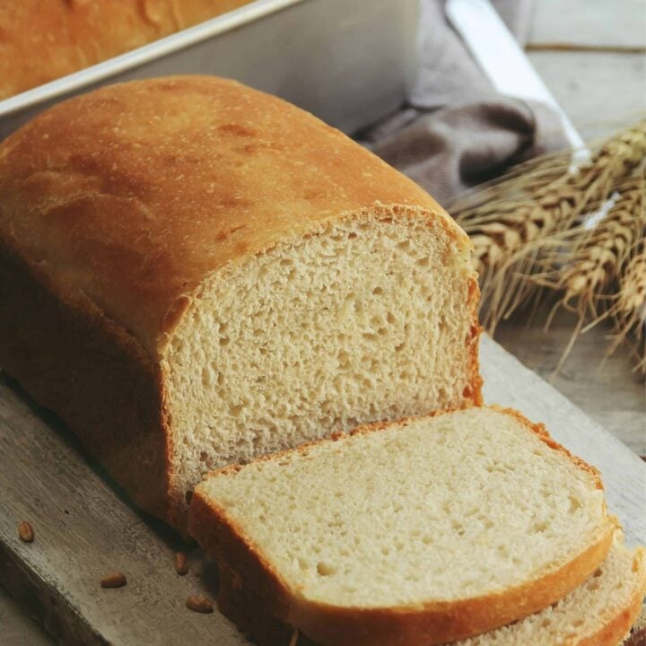 Fresh milled bread on a cutting board with another loaf in a pan behind it.