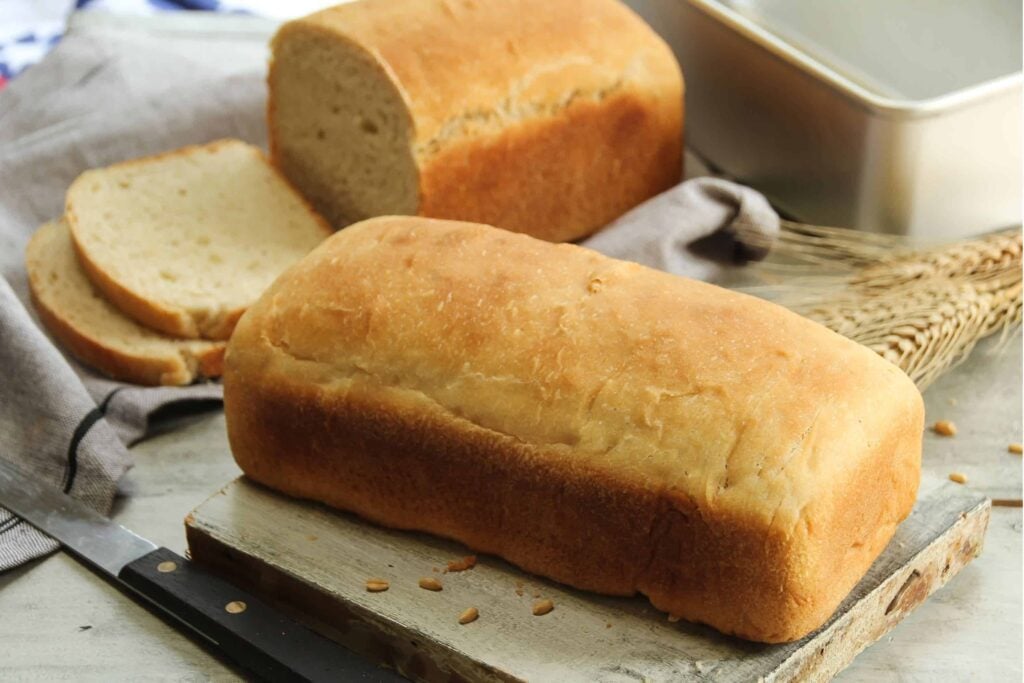 Loaf of fresh milled bread with a second, sliced loaf and pan in the background.