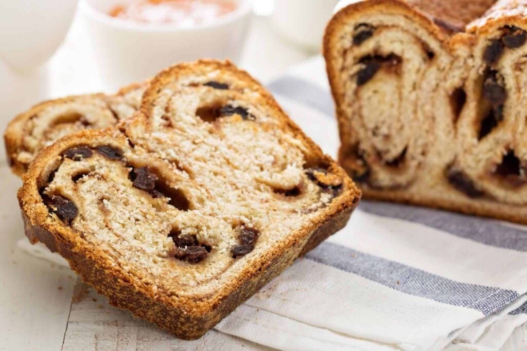 Whole wheat cinnamon raisin loaf sliced on a blue and white tea towel