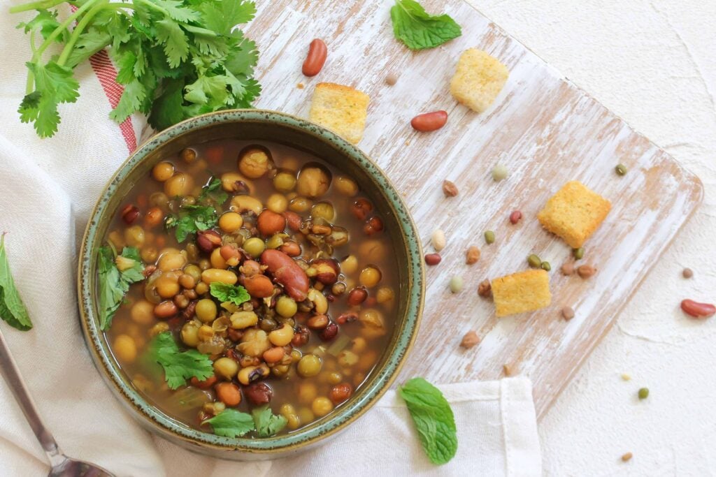 Cozy bean soup with fresh herbs and croutons on a wooden cutting board.