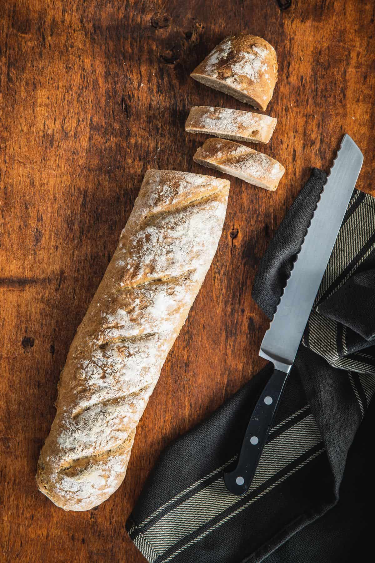 Whole wheat baguette cut into slices on a wooden surface.