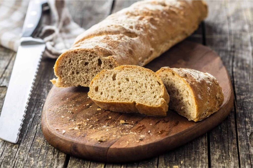 Whole wheat baguettes sliced with a knife and tea towel beside.