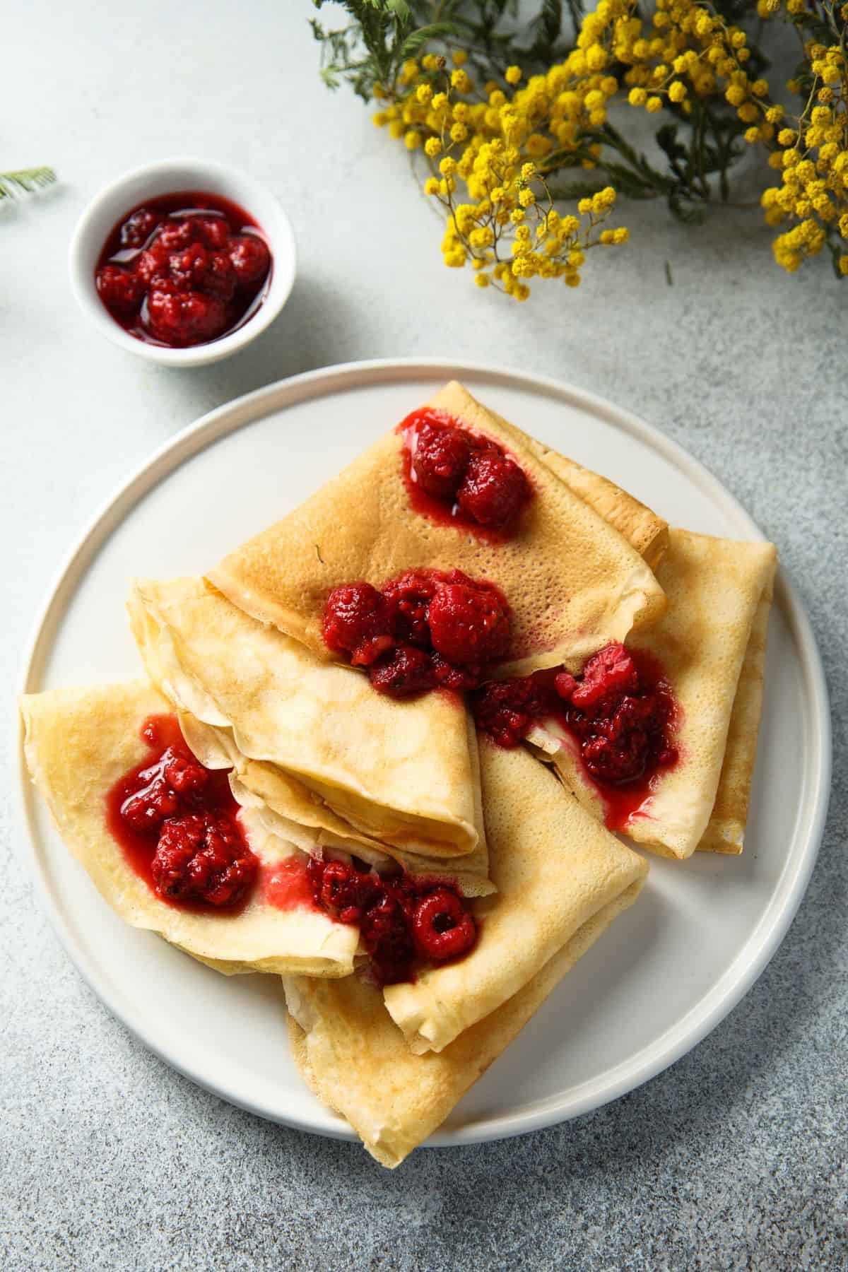 Sourdough crepe recipe with raspberry filling beside yellow flowers.