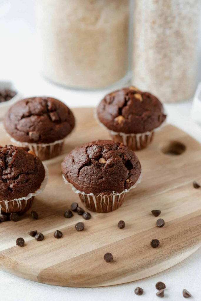 Gooey whole wheat chocolate muffins on a cutting board with chocolate chips