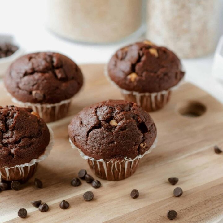 Gooey whole wheat chocolate muffins on a cutting board with chocolate chips