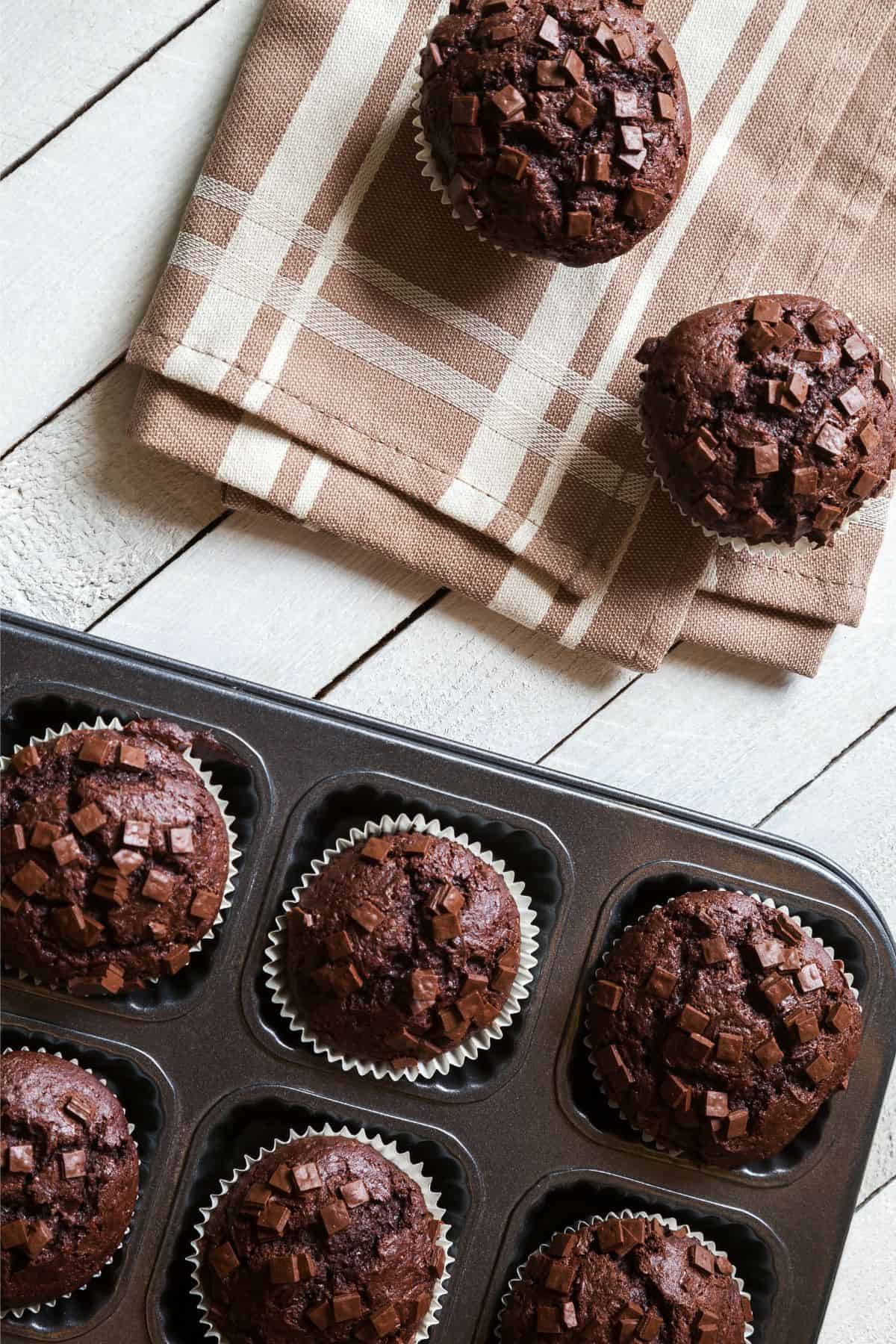 Freshly milled chocolate zucchini muffins in a tin and on a tea towel