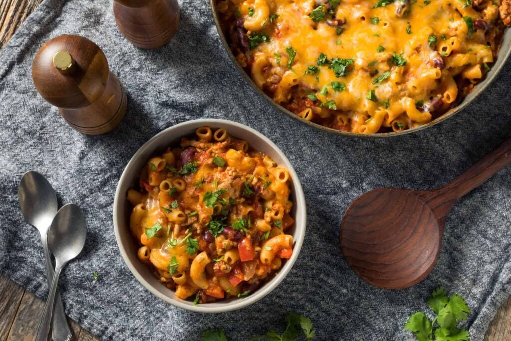 turkey chili mac in a bowl on a set table beside a skillet of the same.