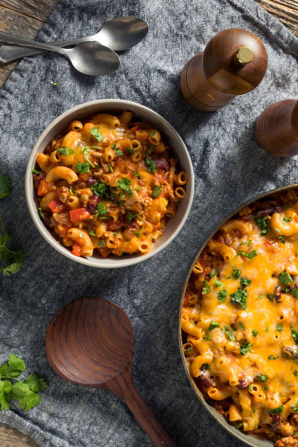 cheesy turkey taco chili mac in a bowl topped with herbs beside a skillet of the same