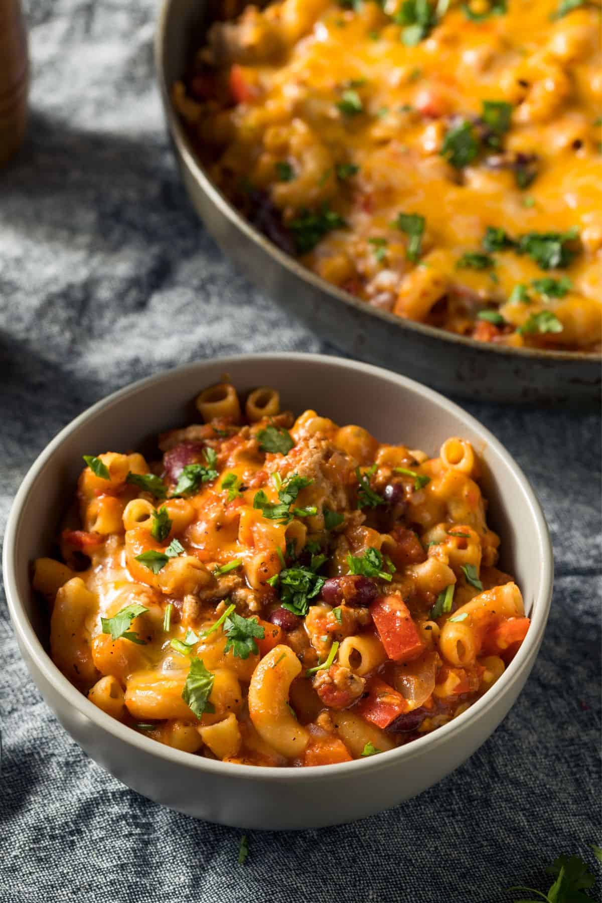 Bowl of cheesy turkey taco chili mac with a skillet of the same in the background.